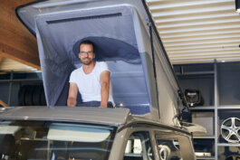 Craig Kammeyer sitting in the roof tent of Custom Bus Fahrzeugbau GmbH & Co. KG by Alex Sobotta Alex Sobotta Fotograf