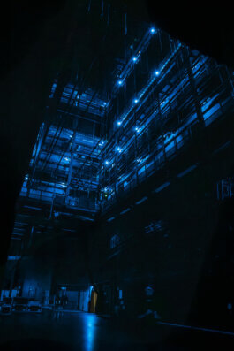 Ein geheimnisvoller Bühnenraum am Potsdamer Platz Theater, eingefangen von Alex Sobotta Fotografie: Blaues Licht durchdringt die Dunkelheit und taucht die sichtbaren Metallgerüste, herabhängenden Kabel und technische Ausrüstung in eine kühle Stimmung. Die hohe Decke verstärkt das industrielle, dramatische Ambiente der Szene. Im Hintergrund verliert sich der Raum in Schatten – kein Mensch ist zu sehen; nur das sorgfältig arrangierte Bühnenbild erzählt seine eigene Geschichte. This cinematic backstage photo by Alex Sobotta shows dramatic lighting and intricate stage equipment at Potsdamer Platz Theater. Industrial details create a moody atmosphere for documentary photography lovers. Alex Sobotta Fotograf