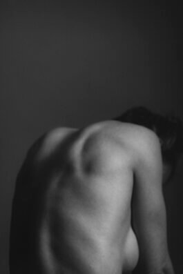 Fotografie von Alex Sobotta: Schwarzweiß-Porträt der Rückansicht eines Models namens Clraissa. Ihr nackter Rücken und die Schulter sind sichtbar, ihr Kopf ist nach unten und vom Objektiv abgewandt. Dramatisches Licht betont Muskeln vor schlichtem Studiohintergrund. Photo by Alex Sobotta shows a studio black and white portrait highlighting the models bare back in soft lighting. Alex Sobotta Fotograf