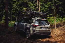 Fotografie von Alex Sobotta: Ein silberner 2025 Subaru Forester SUV mit Dachzelt steht im lichten Wald. Sonnenstrahlen dringen durch hohe Bäume, reflektieren auf Lack und Fenstern. Das Fahrzeug wirkt bereit für Abenteuer – Natur, Freiheit, Entdeckung im Fokus. The photo shows a modern Subaru Forester with rooftop tent in a scenic forest camping setup. Ideal image for outdoor adventure and car camping themes. Alex Sobotta Fotograf