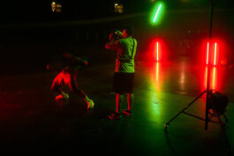Aron lehnt sich dramatisch zurück, sein Gesicht entschlossen, grelles Rot und Grün tauchen die dunkle, weite Halle des Velodroms in filmisches Licht. Fotografie von Alex Sobotta. Alex Sobotta Fotograf