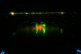 Dunkle Halle, vermutlich das Velodrom, mit drei leuchtenden Neonröhren in Grün, Rot und Gelb, die den Boden akzentuieren. Im Hintergrund schwache Sitzreihen und Schatten. Fotografie von Alex Sobotta. Neon lights highlight the empty arena floor. Alex Sobotta Fotograf