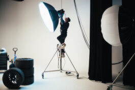 Eine Person balanciert konzentriert auf einer hohen Leiter und richtet ein großes Studio-Licht (