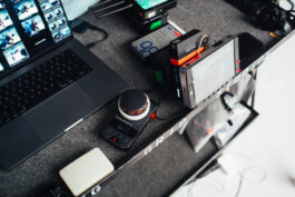 Ein dokumentarisches Foto von Alex Sobotta zeigt einen Fotografen-Arbeitsplatz: Laptop mit Fotovorschauen, digitaler Audiorekorder, tragbarer Monitor und Elektronik akribisch auf grauem Tisch arrangiert, sanftes Licht betont Details. Photographic BTS workflow. Photographie setup. Alex Sobotta Fotograf