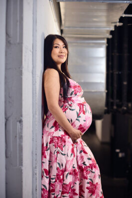 Jiaoying Summers im geblümten Kleid im Backstage-Gang des Punchline Club, an eine weiße Wand gelehnt, helles Tageslicht von der Seite. Alex Sobotta Fotograf