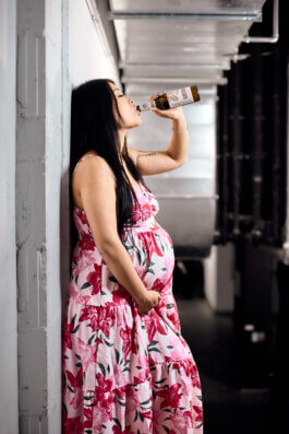 Jiaoying Summers setzt im Backstage-Gang eine Flasche alkoholfreies Bier an, angelehnt an die weiße Wand, Tageslicht von hinten. Alex Sobotta Fotograf