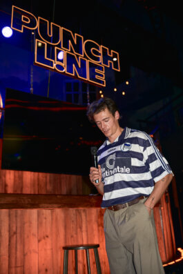 Mario Adrion auf der Bühne des Punchline Club mit dem Mikrofon in der Hand, über ihm der beleuchtete Punchline-Schriftzug. Alex Sobotta Fotograf