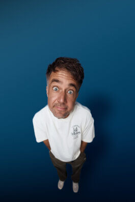 Moritz Hohl vor blauem Hintergrund, mit kurzen braunen Haaren und blauen Augen, im weißen Adidas-Shirt, brauner Hose und weißen Schuhen. Mit dem Ultraweitwinkel von oben fotografiert, er blickt mit offenem Gesichtsausdruck nach oben in die Kamera. Alex Sobotta Fotograf