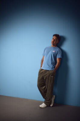 Moritz Hohl lehnt in ganzer Figur an einer blauen Wand, die Beine übereinander geschlagen, entspannte Haltung. Alex Sobotta Fotograf